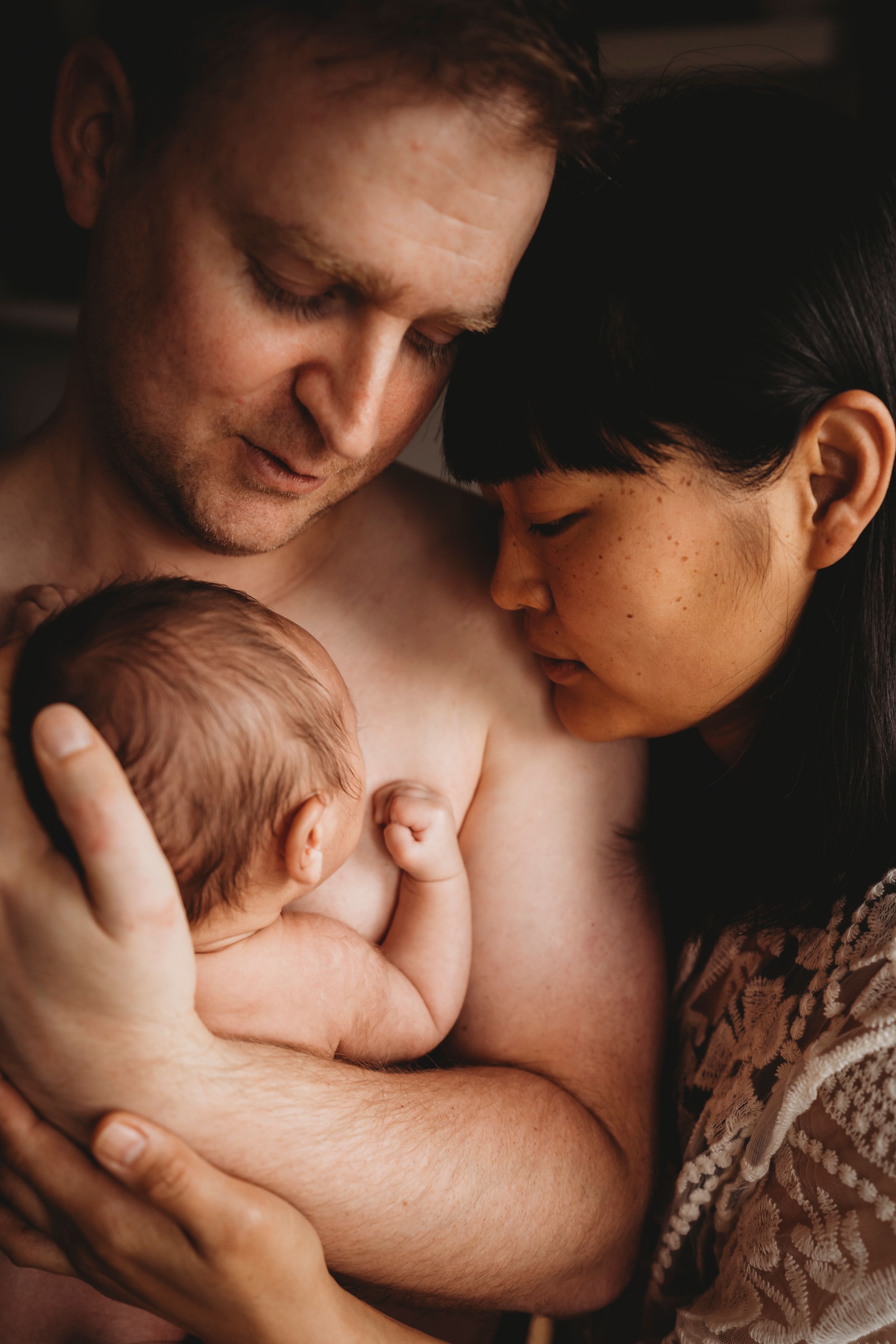 An intimate family portrait showing tender care of a newborn baby in warm lighting.