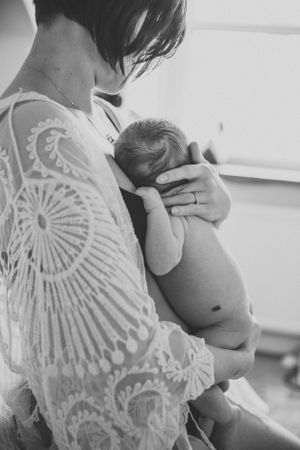 A tender moment of comfort as a newborn baby is cradled in loving arms wearing a lacy white top.