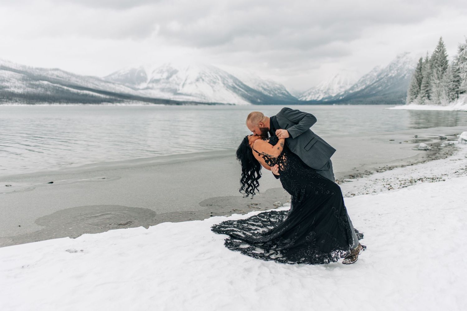 Bride and groom sitting on rocky lakeshore with mountain reflections and autumn foliage at Glacier National Park.
