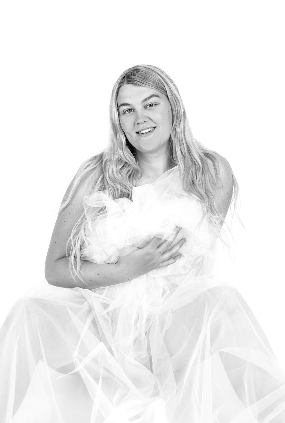 Black and white portrait of a smiling blonde woman in a white flowing gown holding soft tulle fabric.