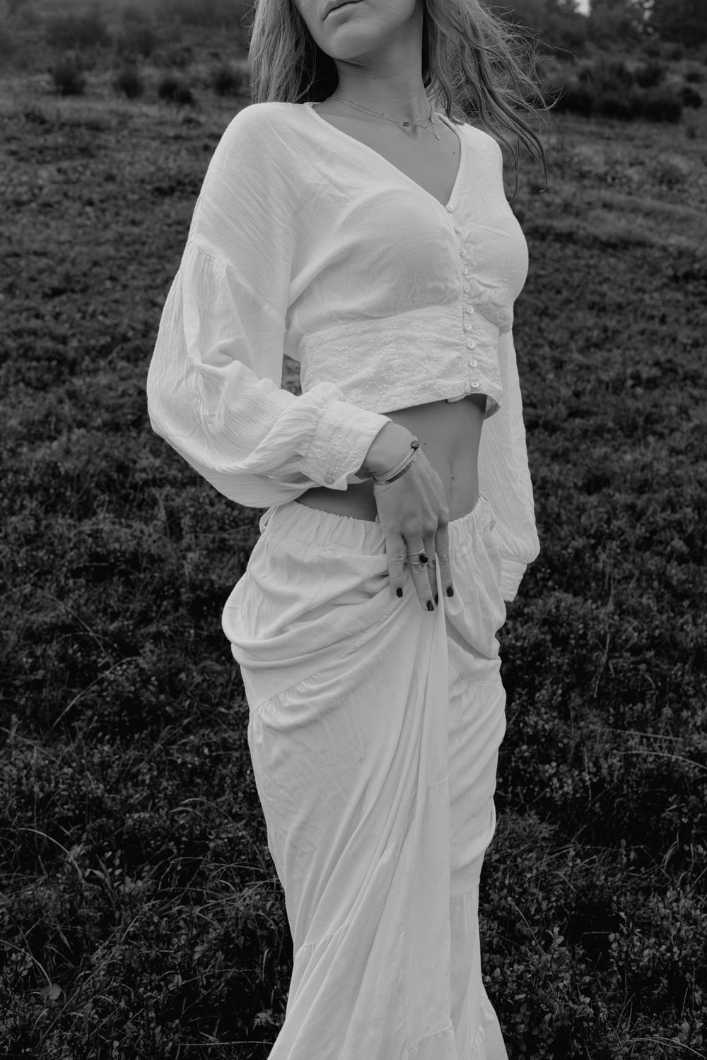 Woman in white cropped blouse and maxi skirt posing outdoors in black and white photo.