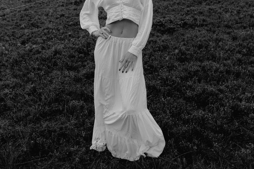 Black and white photo of a woman in a white crop top and maxi skirt standing in a field.