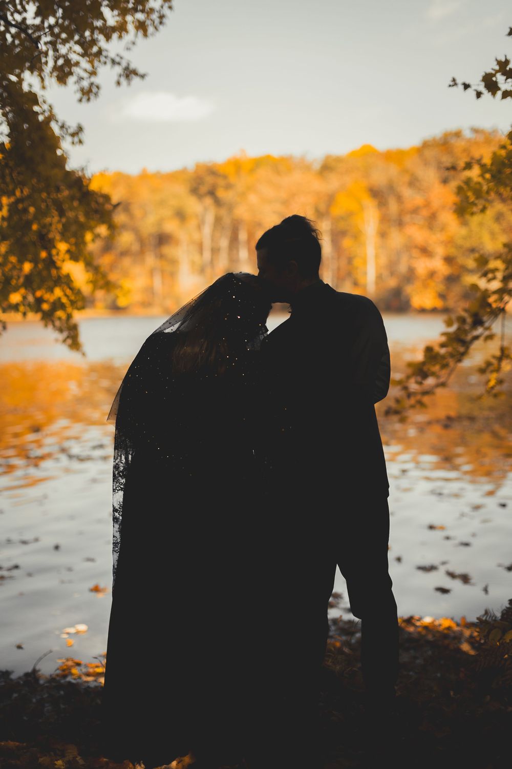 Silhouette of a couple kissing by a lake surrounded by vibrant autumn foliage in warm golden tones at Seneca Creek State Park