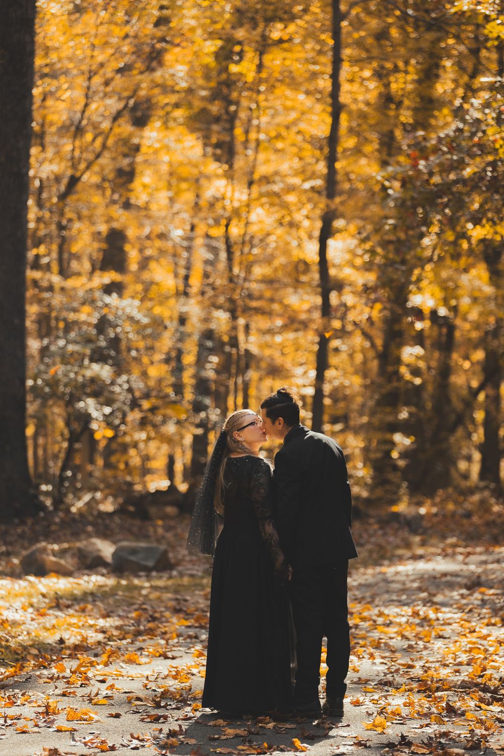 Couple sharing a romantic kiss in an autumn forest, surrounded by vibrant golden yellow foliage and fallen leaves.