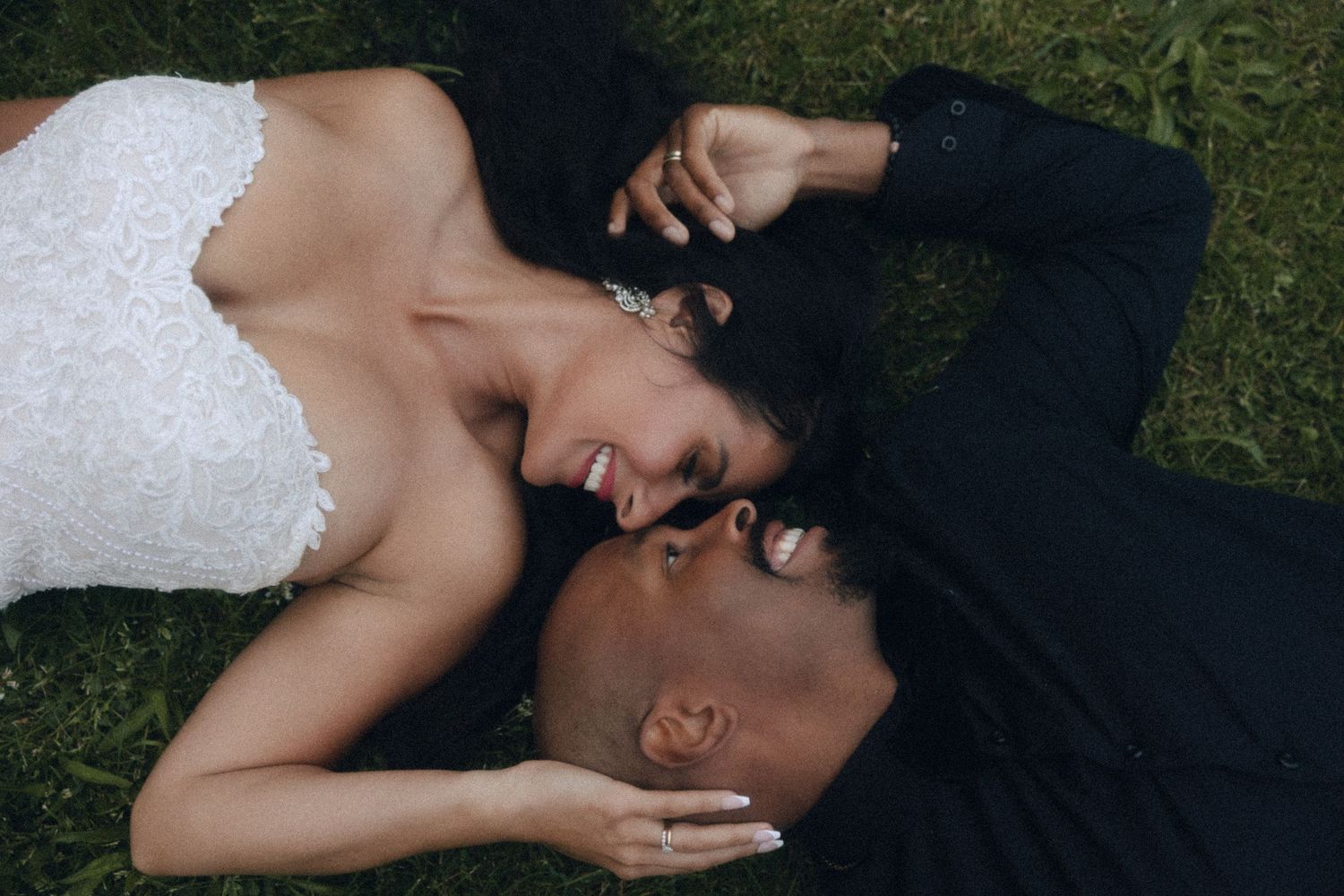 Couple lying close together on green grass, sharing an intimate moment while wearing black and white outfits.