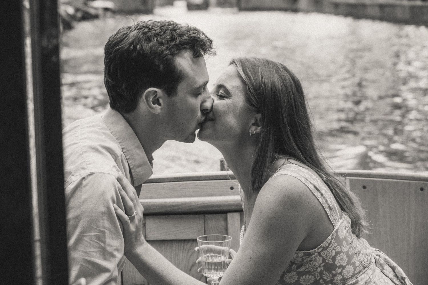 Black and white photo of a couple sharing a romantic kiss outdoors near a wooden bench.