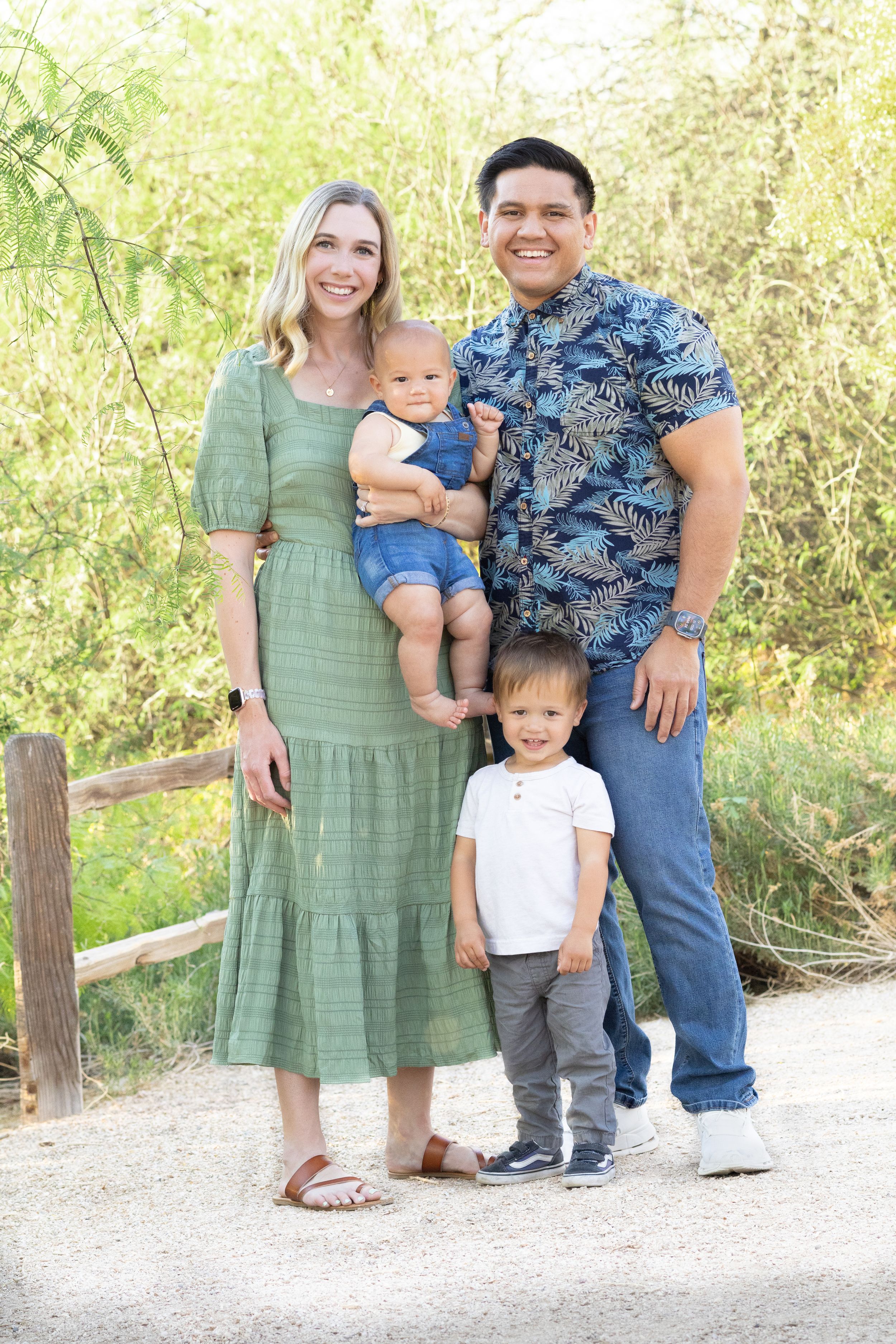 Light and airy image of a family of 4 at the Riparian Preserve in Gilbert, Arizona standing in front of greenery brush and a wooden fence.