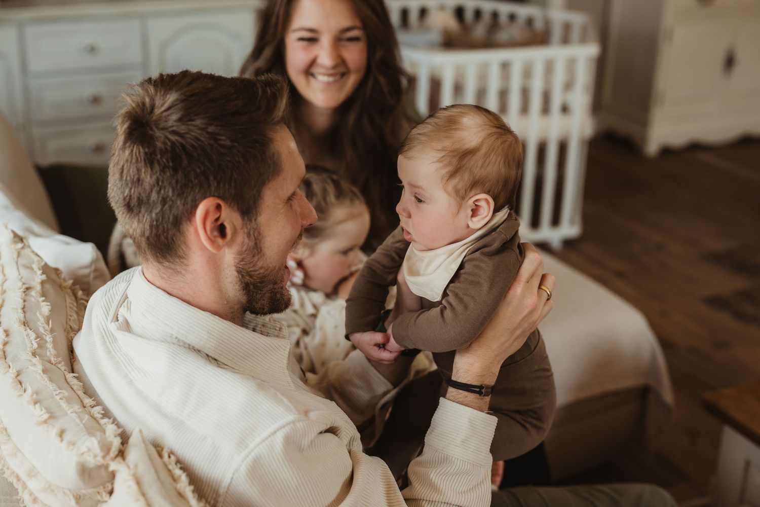 Happy family moment with parents smiling at baby in cozy nursery room setting.