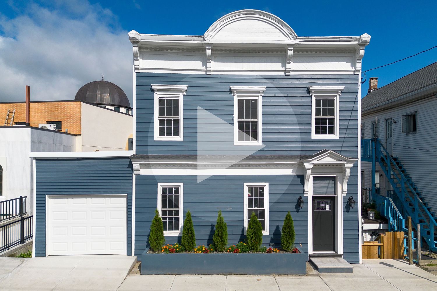 Renovated blue two-story colonial home with white trim, garage, and decorative landscaping.