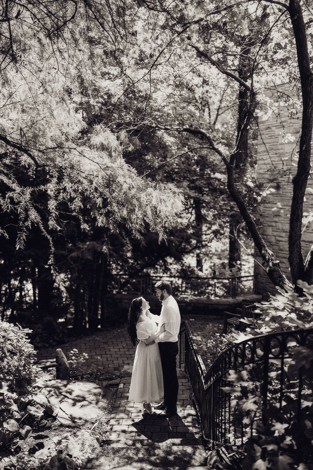 Black and white photo of a romantic couple embracing in a lush garden setting.