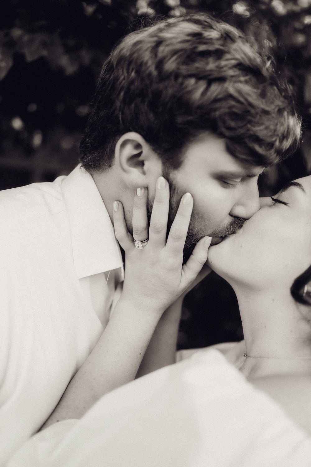 Black and white photo of a couple sharing a romantic kiss, with an engagement ring visible on her hand.