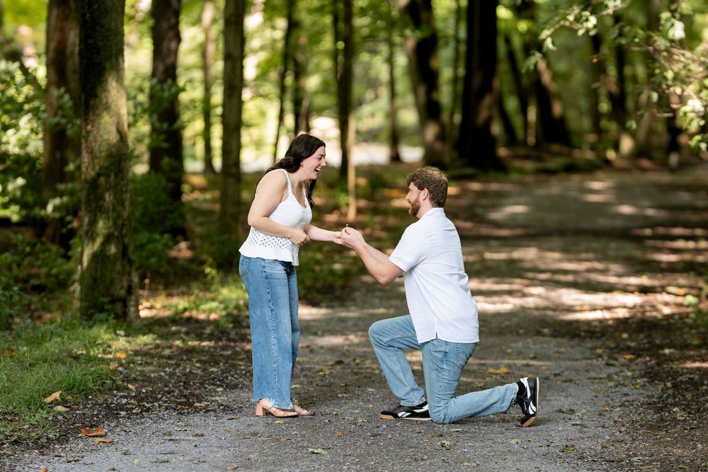 A man on one knee holds his partners hands during a marriage proposal outdoors.
