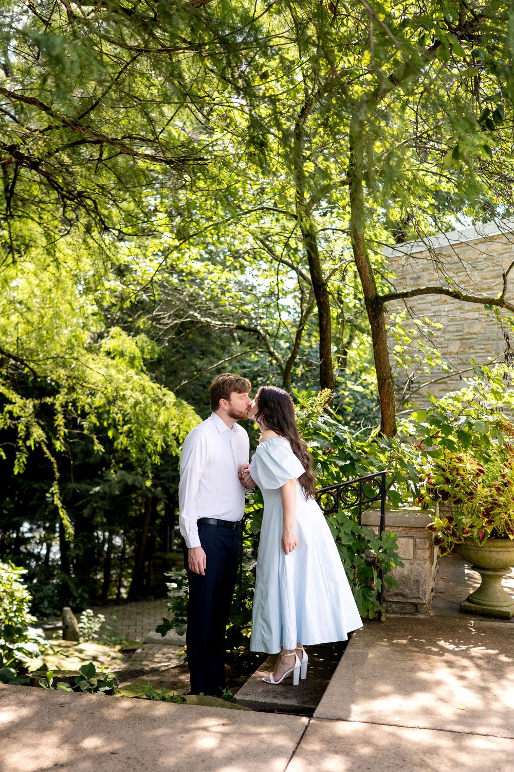 Couple sharing a kiss on a garden path surrounded by vibrant green foliage.