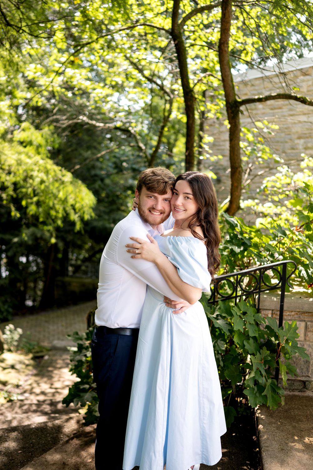 Smiling couple embracing in a beautiful garden with lush green trees.