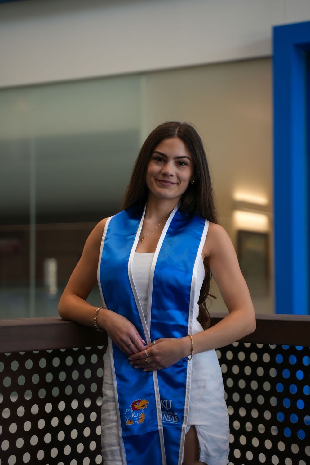 Young woman in graduation stole smiling at camera in modern building.