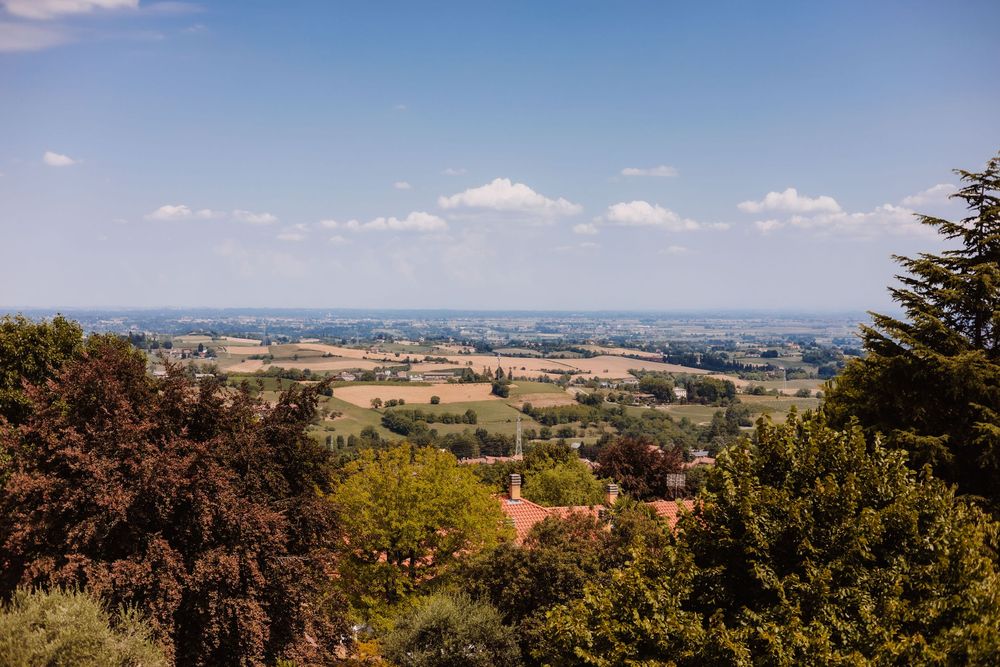 Panoramic view of rolling Tuscan countryside with lush green trees, farmlands, and a clear blue sky.