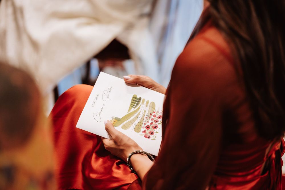 Woman in red dress holding a decorative wedding program card with floral illustration at a ceremony.