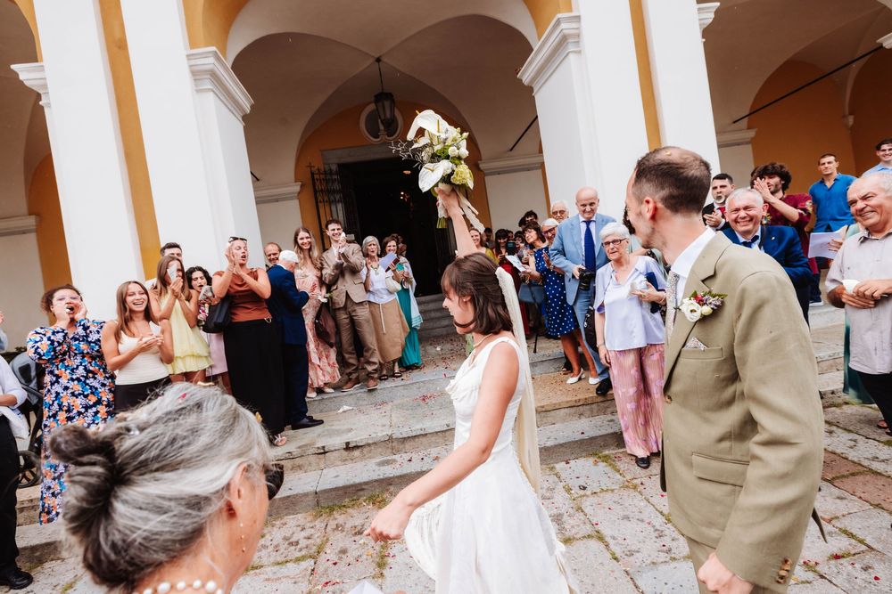 Newlywed couple exits church greeted by cheering guests at outdoor wedding ceremony.