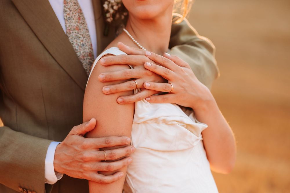 Close-up of bride and groom embracing, showcasing wedding rings on their hands during an outdoor ceremony.