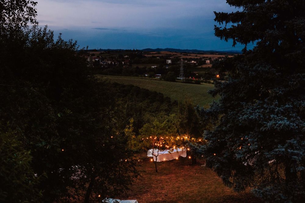 Aerial twilight view of an outdoor wedding reception with string lights, surrounded by trees and countryside.