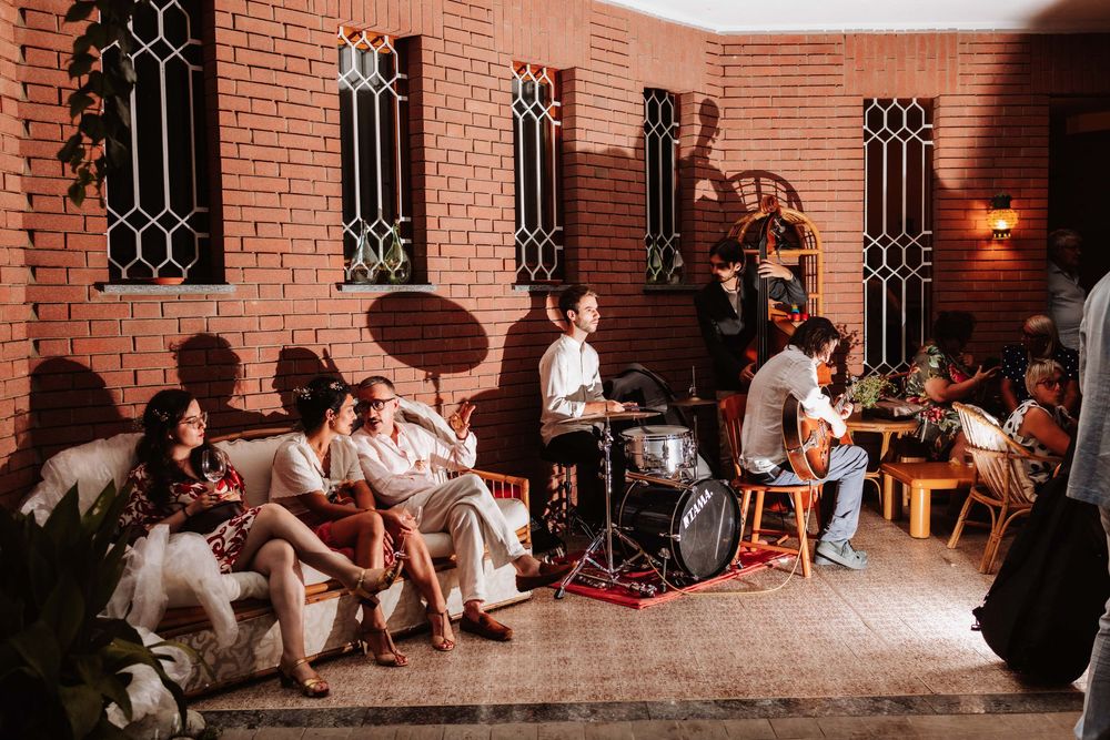 A lively outdoor gathering with guests relaxing on a patio while a live band performs against a brick wall backdrop.