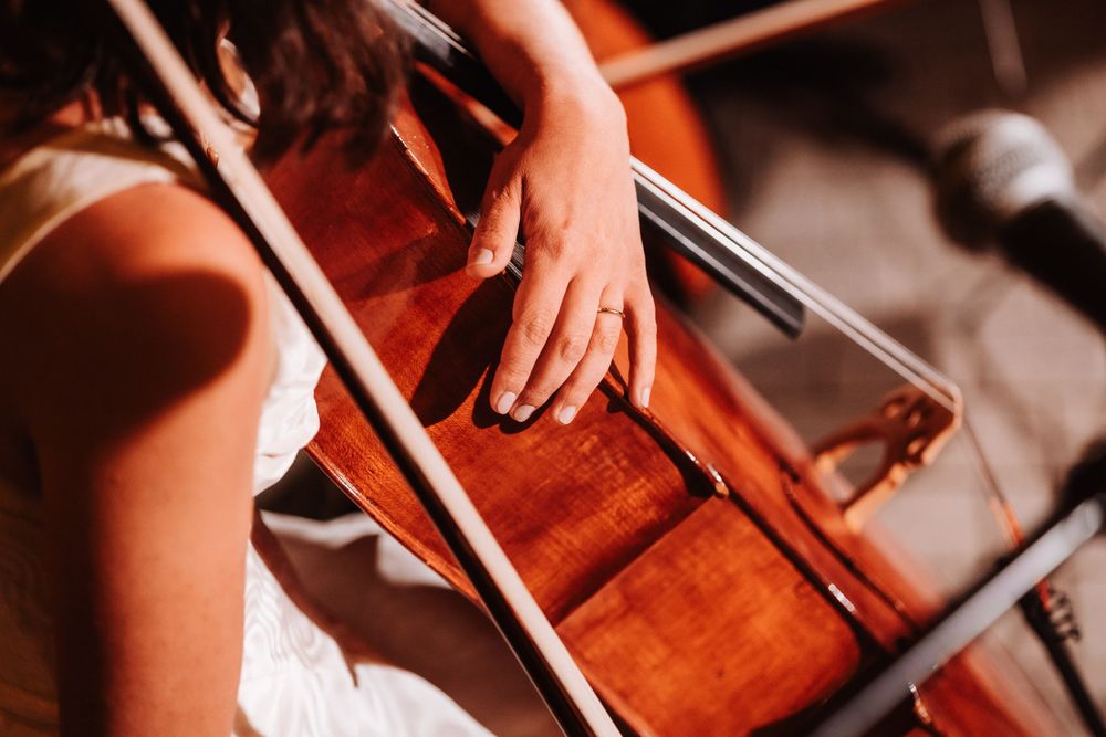 Close-up of a musician playing cello, with bow and strings visible, wearing a white dress and ring.