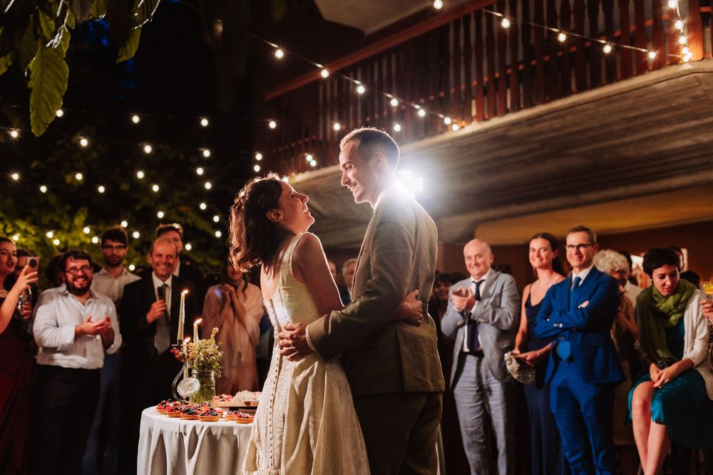 Bride and groom share first dance surrounded by applauding guests under warm string lights at an outdoor wedding reception.