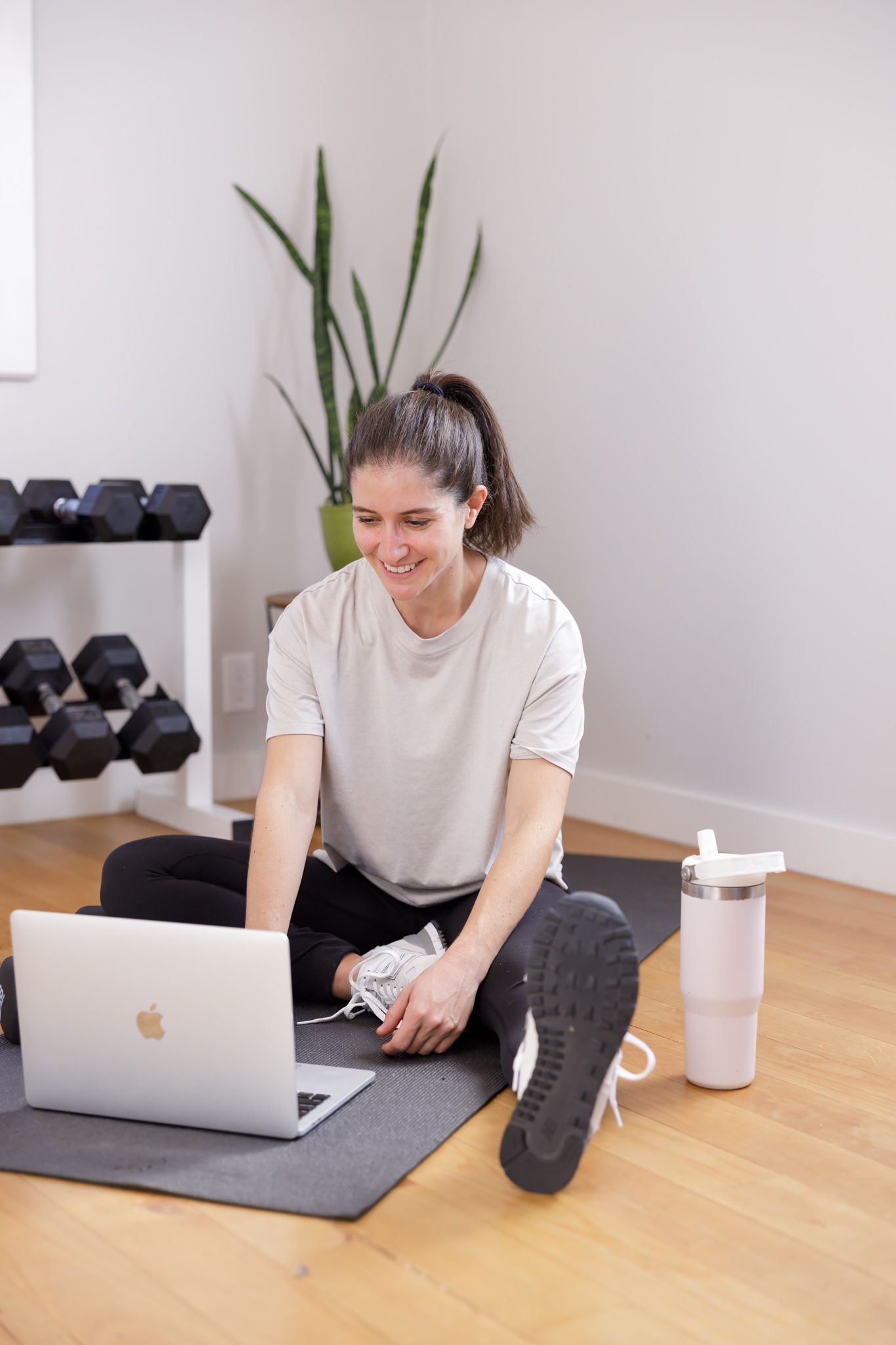in home personal trainer in Seattle, WA branding female sitting on yoga mat on floor looking through computer library of home workout videos