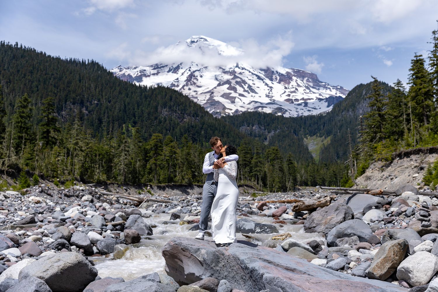 Person posing at the Mt. Rainier National Park entrance gate surrounded by lush green forest trees.
