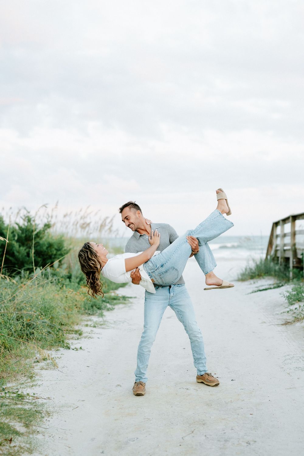 Couple dancing on a sandy beach path, man dipping woman with sea oats and ocean in the background.