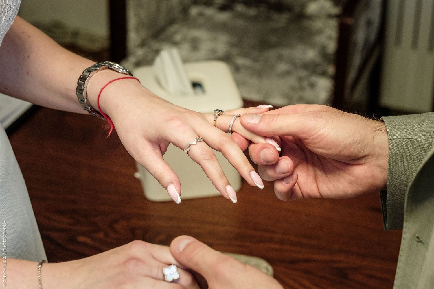 A groom placing a wedding ring on the bride's finger during a ceremony, bride wearing a red bracelet.
