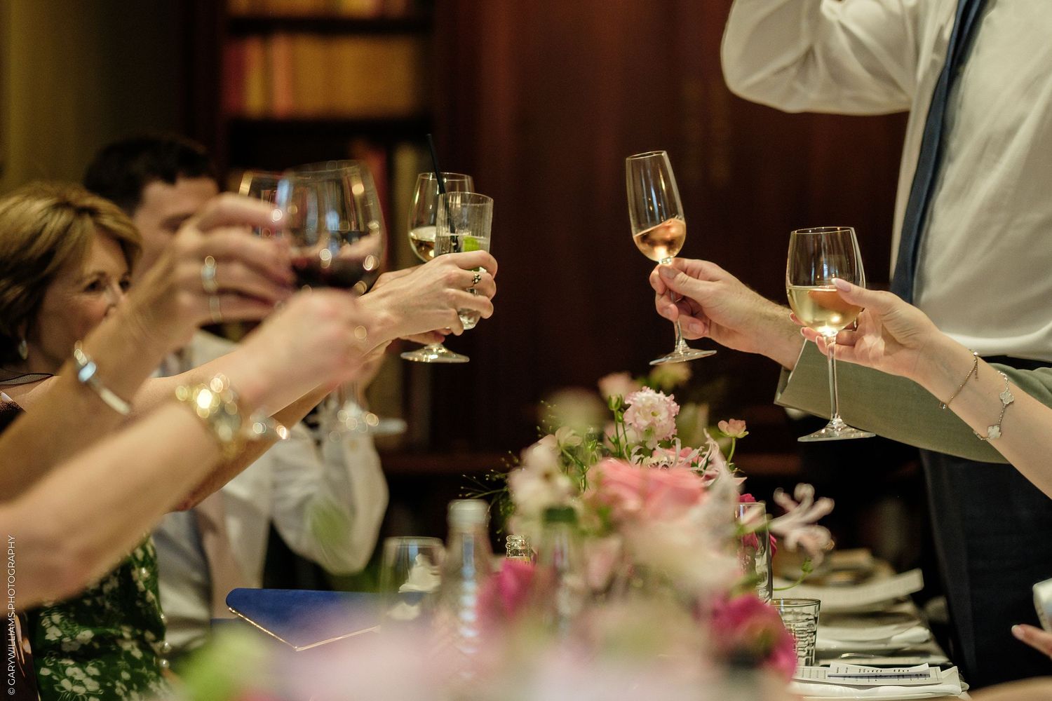 Guests raising wine and champagne glasses in a toast at an elegant wedding reception dinner table with floral centerpieces.