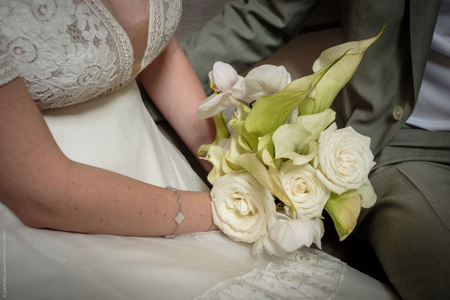 Bride and groom holding a elegant white rose and calla lily wedding bouquet, close-up detail shot.