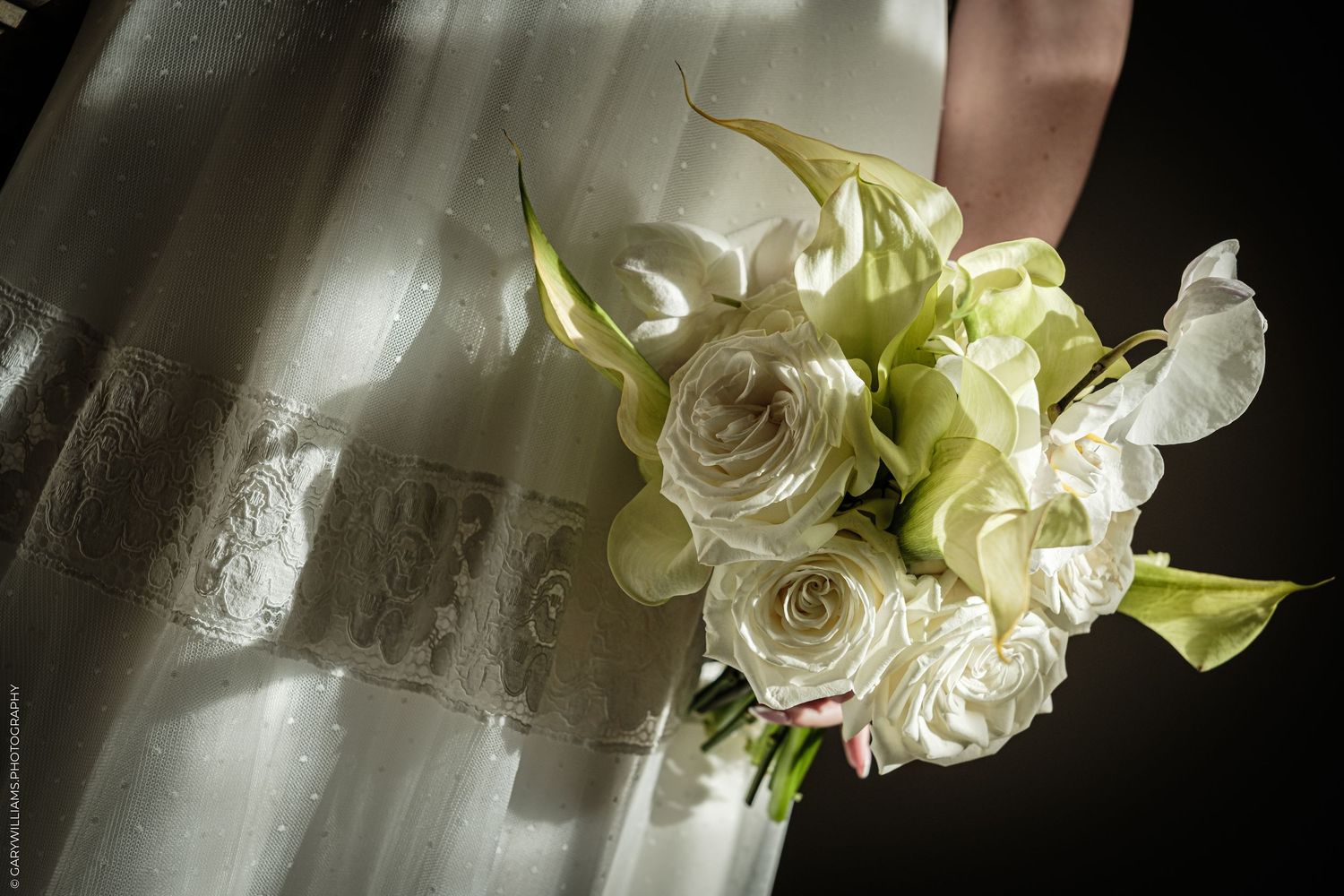 Bride holding a elegant white rose and green calla lily wedding bouquet against a flowing white lace bridal gown.