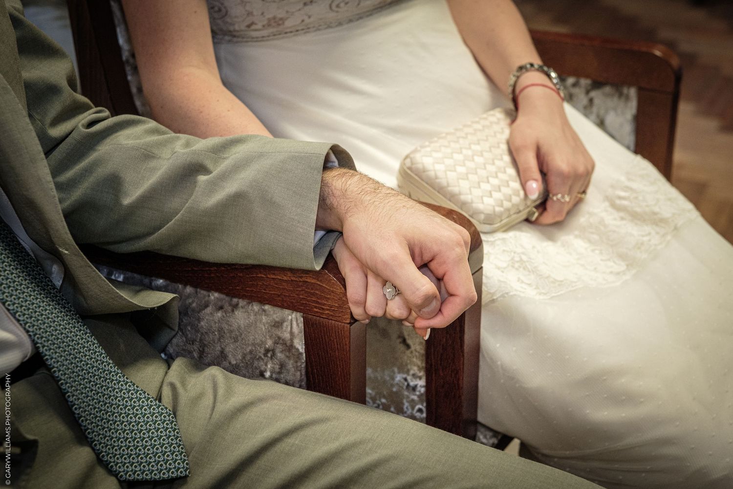 Bride and groom holding hands while seated, wedding dress and suit visible in romantic ceremony moment.