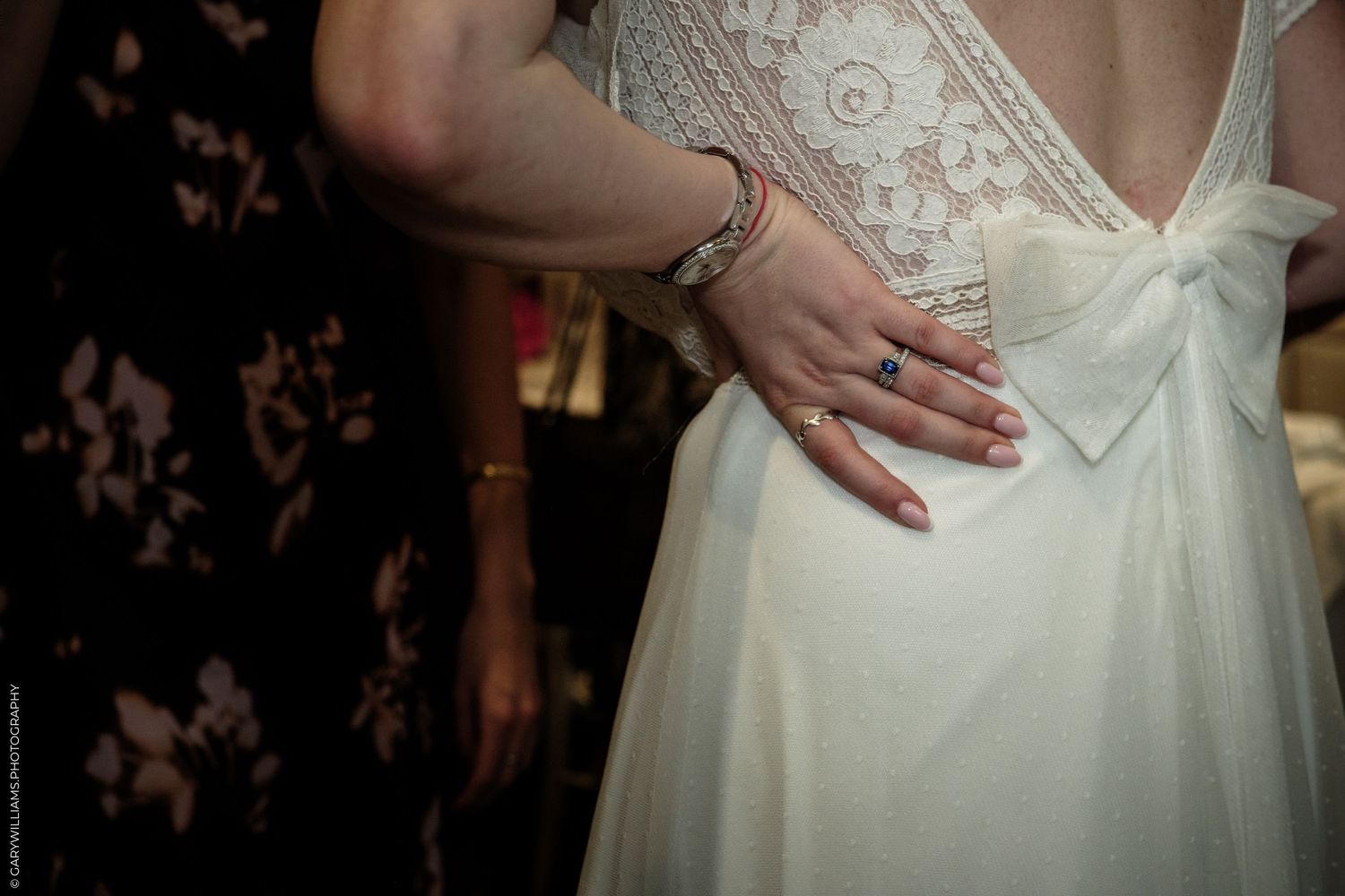 Close-up of a bride in a white lace wedding dress with a bow, showcasing elegant manicured hands and a blue gemstone ring.