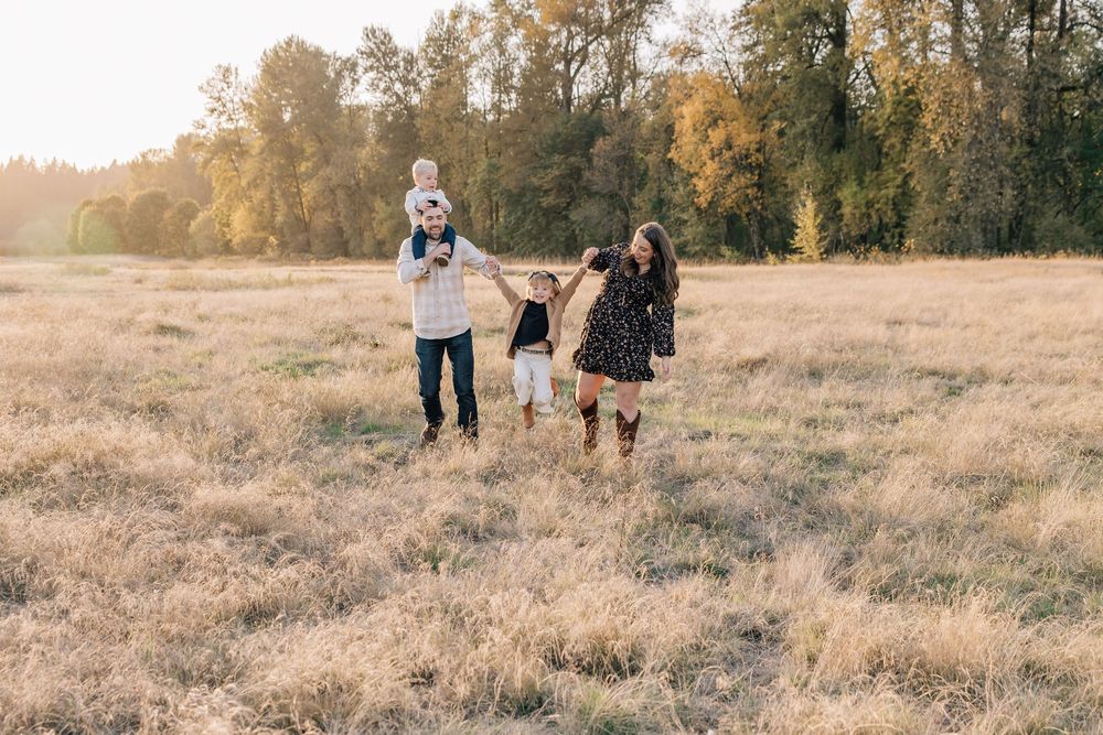 Family of four playing in a golden field during autumn, with trees in the background on a sunny day.