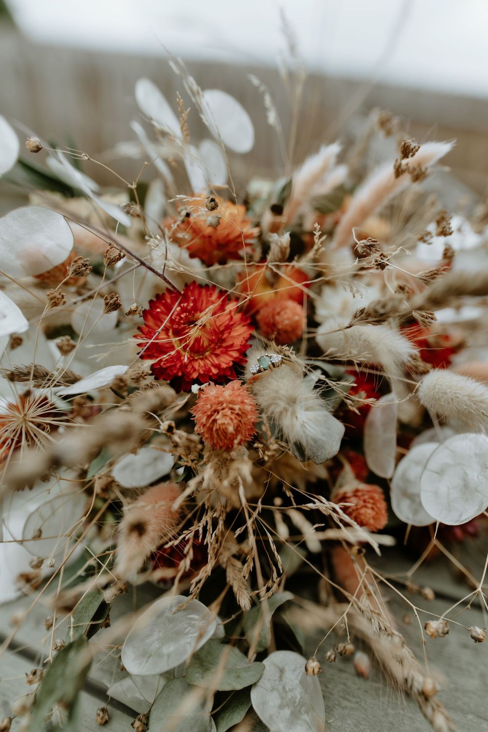 Rustic wedding bouquet with dried red dahlias, pampas grass, eucalyptus, and wildflowers in warm autumn tones.