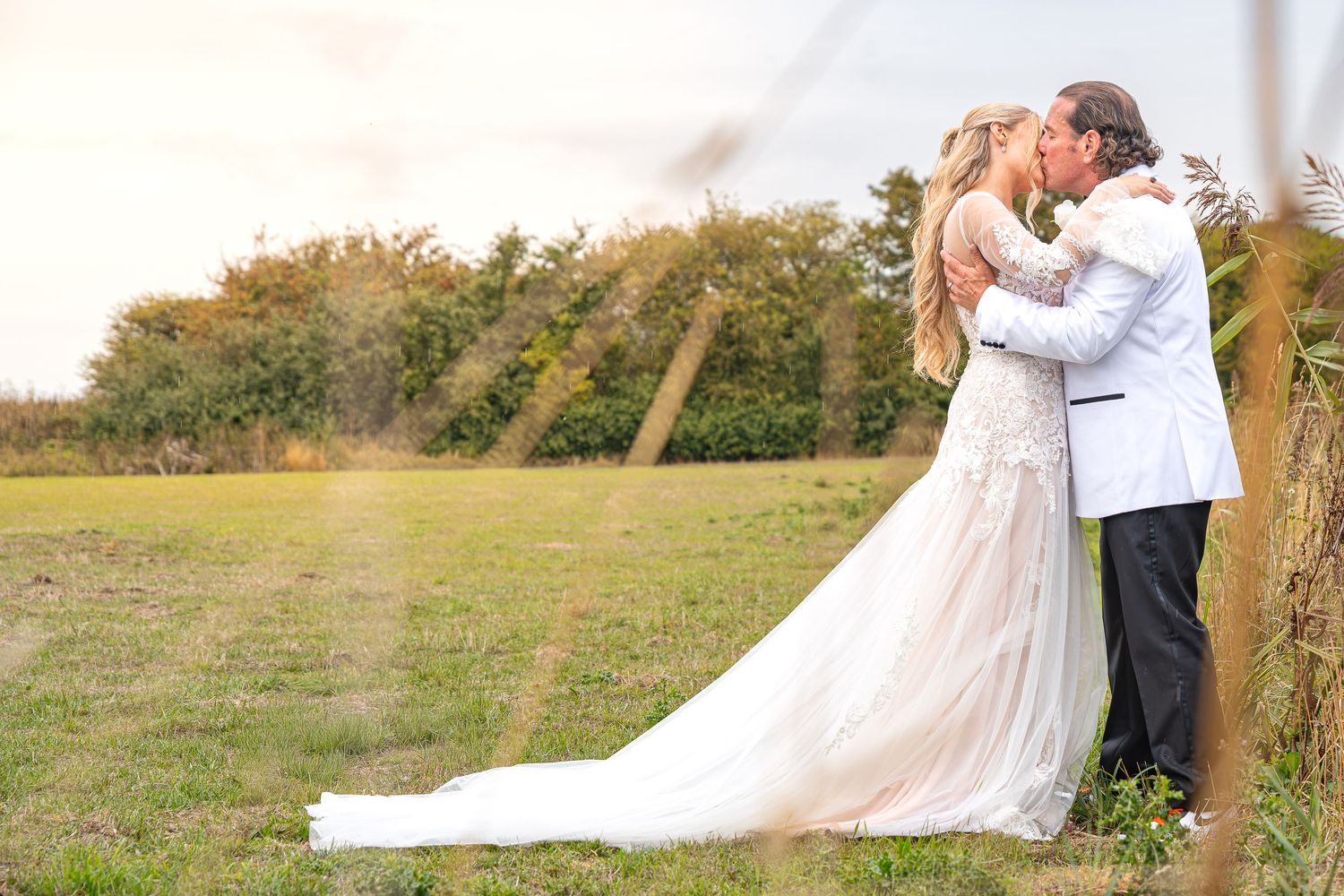 A bride and groom share a romantic kiss in a lush green field, with the bride in a flowing white gown.Yorkshire, Sheffield, Lincolnshire, UK