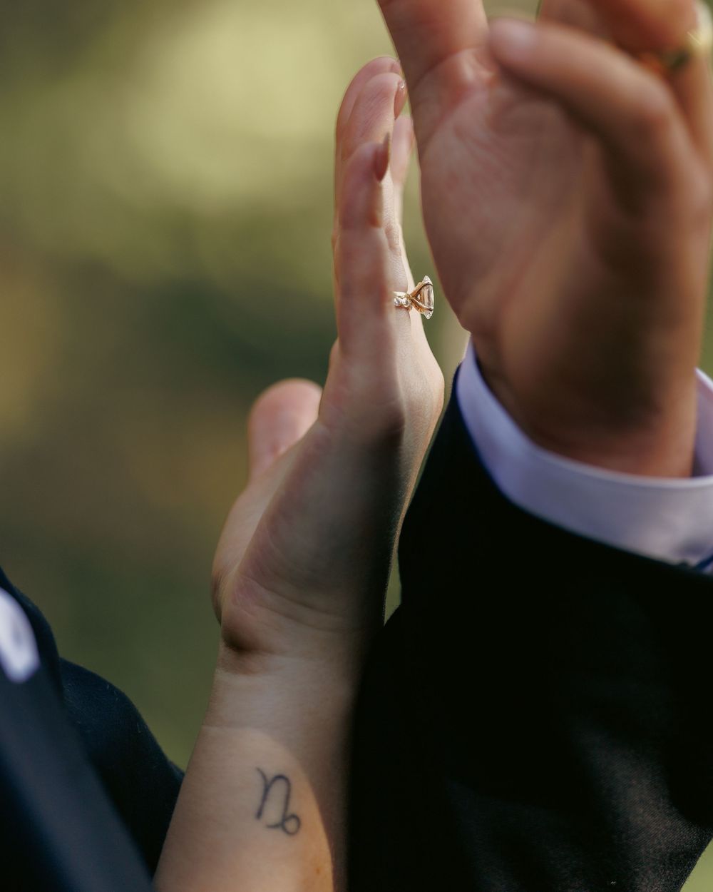 Close-up of bride and groom holding hands, showing Capricorn wrist tattoo and gold ring.
