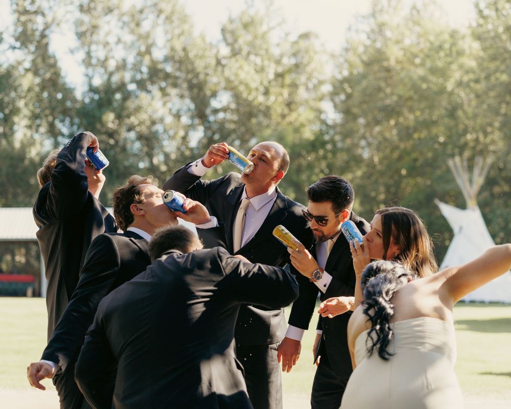 Joyful wedding party celebrating outdoors, drinking and laughing together in sunny garden setting.