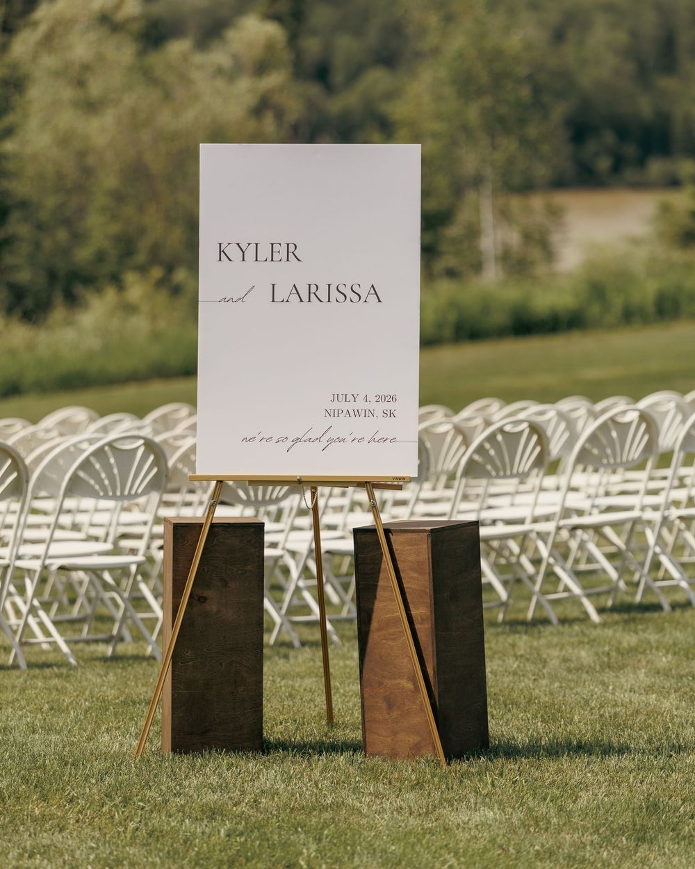 Elegant outdoor wedding welcome sign for Kyler and Larissa on a wooden easel with white chairs.
