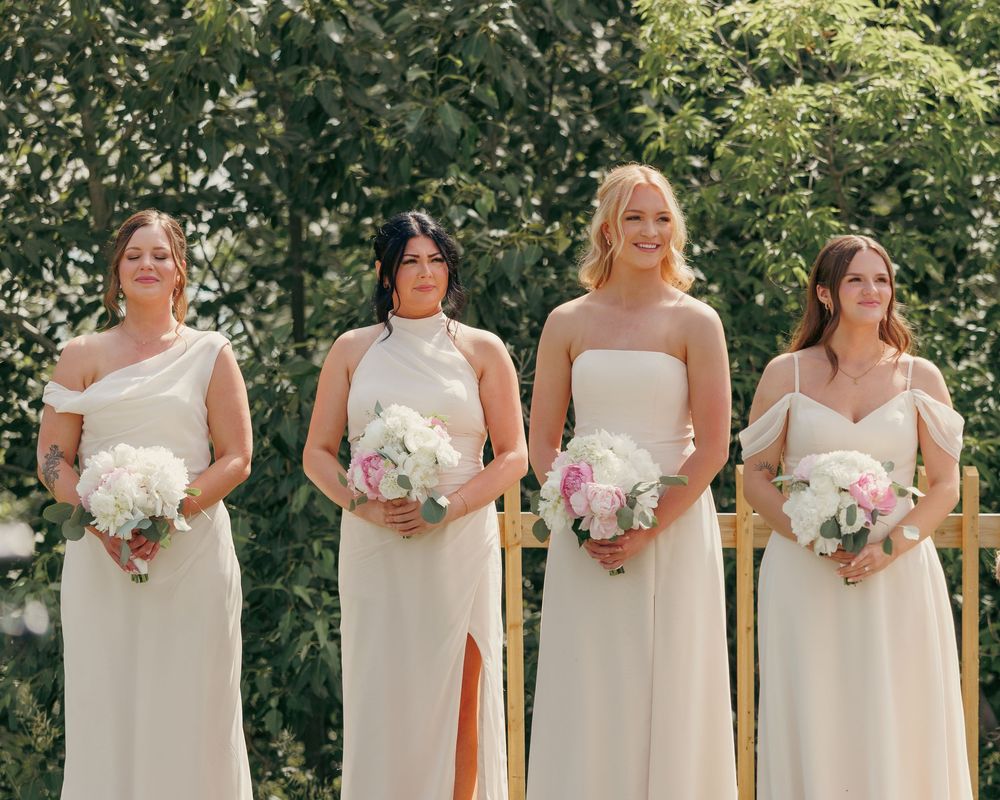 Four bridesmaids in mismatched champagne gowns holding pink and white bouquets outdoors.