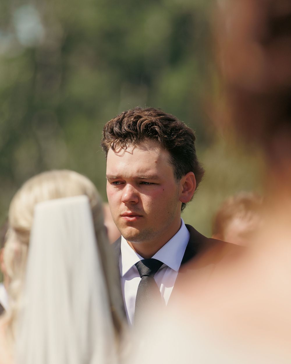 Emotional groom watching bride approach during outdoor wedding ceremony in candid portrait.