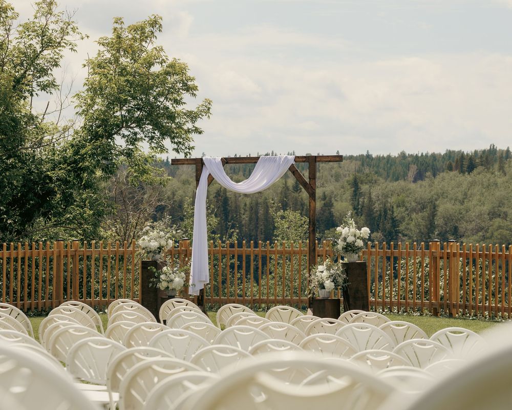 Rustic wooden wedding arch draped with white fabric at an outdoor ceremony with white chairs.