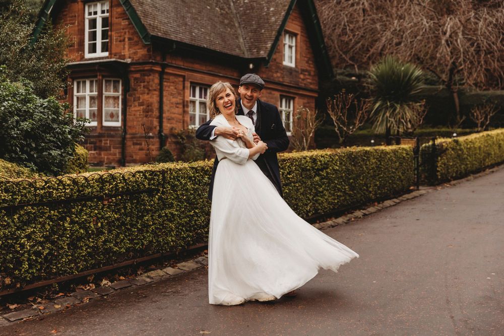 Wedding couple dancing outside red brick Victorian house with manicured hedges.