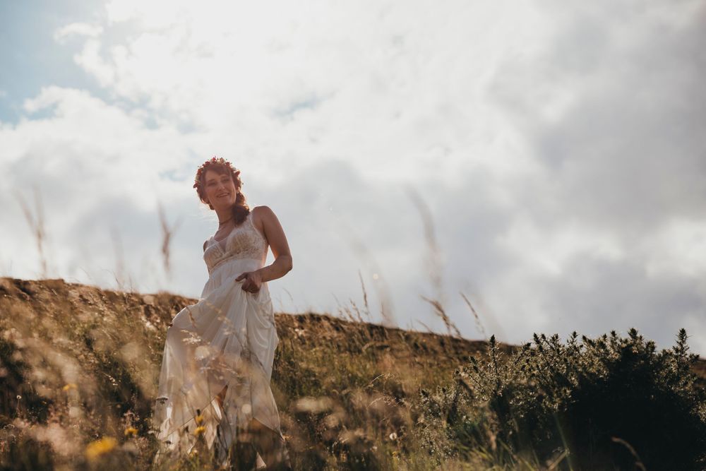 Wedding dress catches wind dramatically against cloudy mountain backdrop.