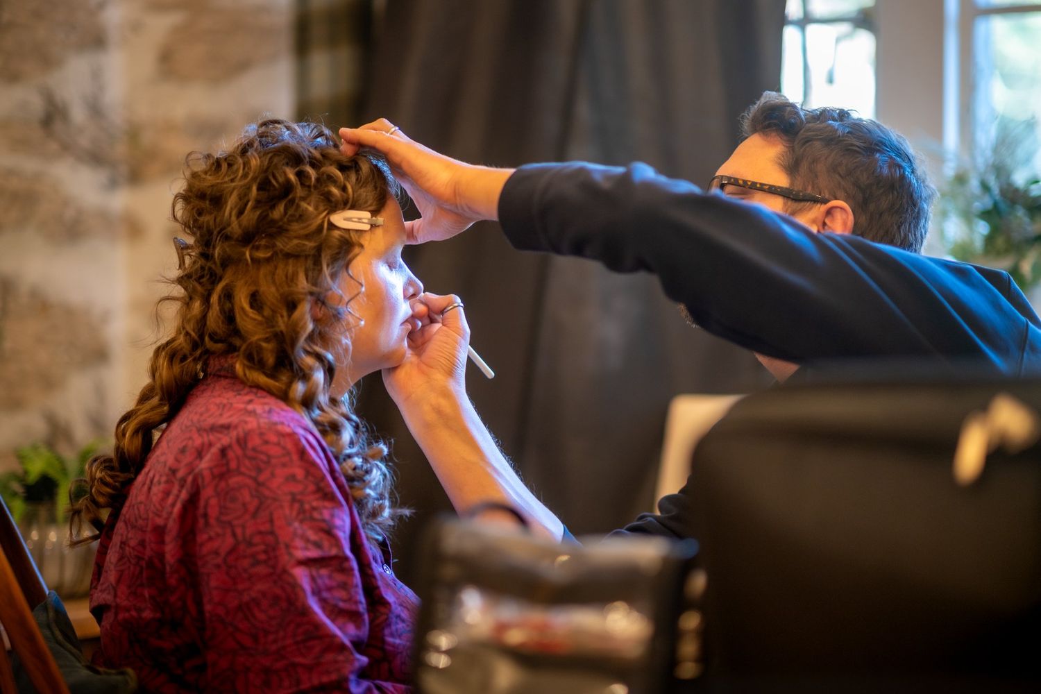 Professional makeup artist applying makeup to a woman with curly hair in a well-lit studio setting.