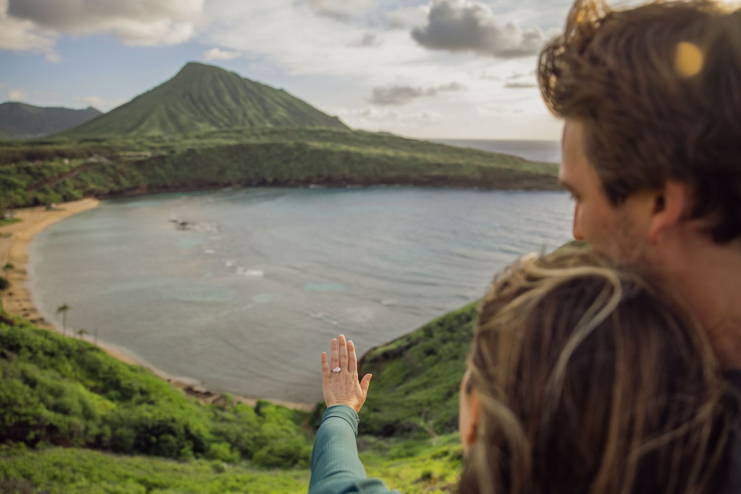 Couple overlooking a stunning Hawaiian bay with lush green mountains and turquoise waters from a scenic overlook.