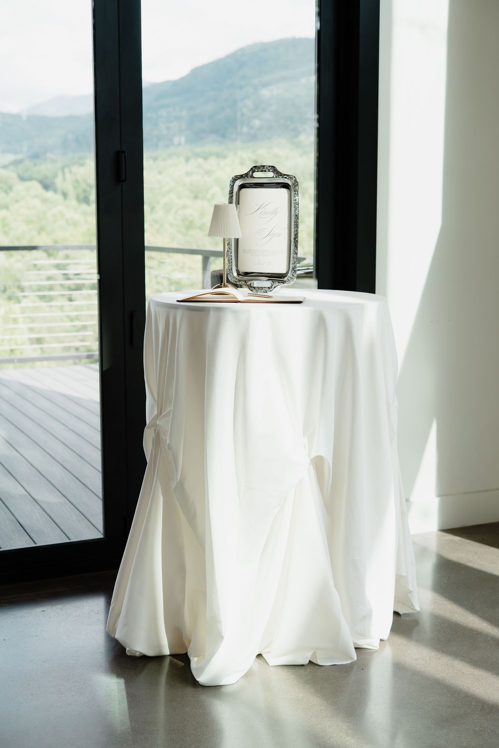 Elegant white cocktail table with silver tray and framed sign, set against floor-to-ceiling windows with mountain views.